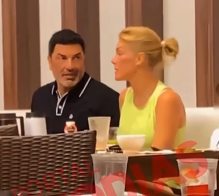 Ana Hickmann e Edu Guedes aparecem juntos sentados em mesa de restaurante. A apresentadora veste uma regata amarela e Edu Guedes camisa preta com detalhes brancos na gola. No fundo há uma imagem dos dois em ensaio fotográfico